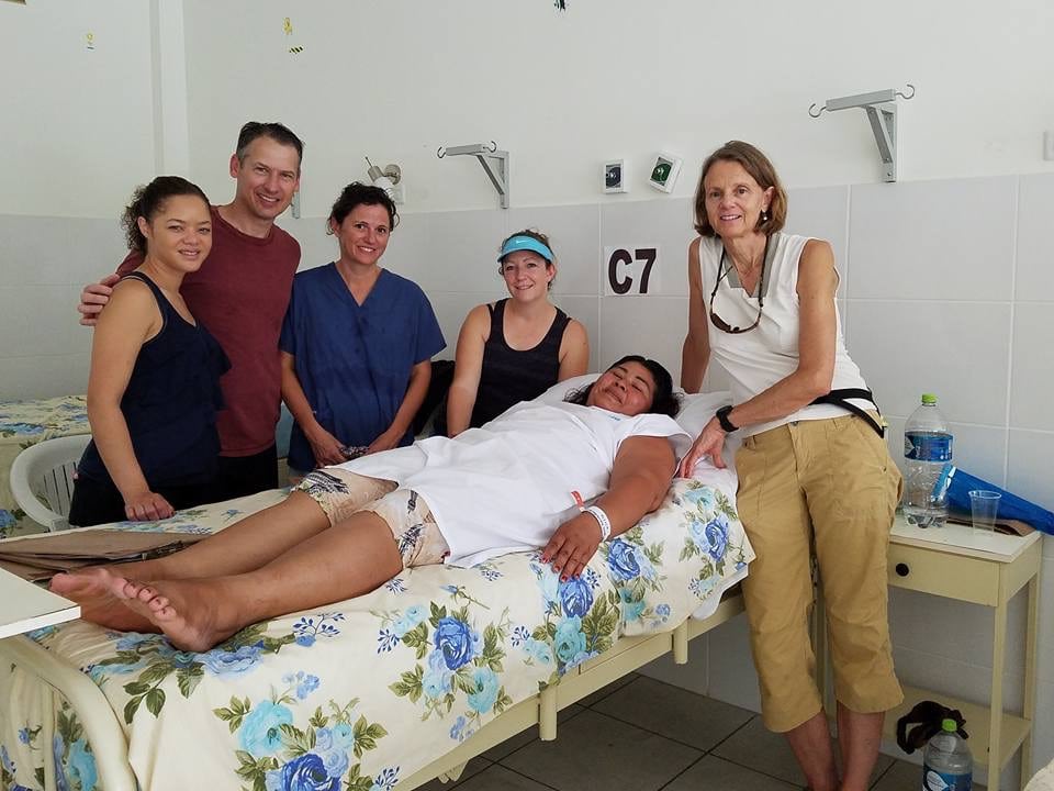 A group of people posing for photos next to a bed in a hospital.