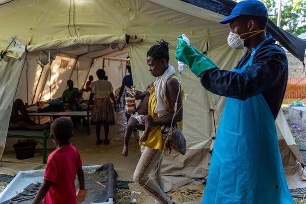 A man with a mask and gloves providing medical care in front of a tent in an underserved community.
