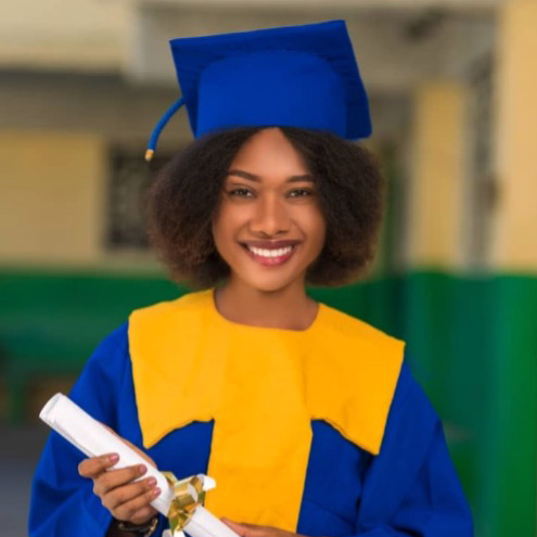 A joyful young woman in a blue and yellow graduation cap and gown, holding a diploma, standing in front of a blurred building.