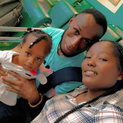 A family of three, including a man, a woman, and a young child, taking a selfie in a waiting area with green seats.